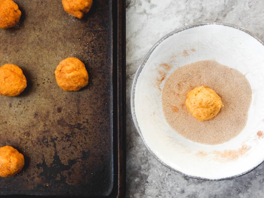 Rolling pumpkin snickerdoodles in cinnamon sugar on white plate