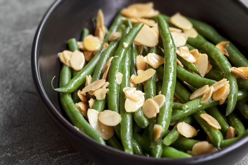 Green beans with toasted almonds, in black bowl over dark slate.