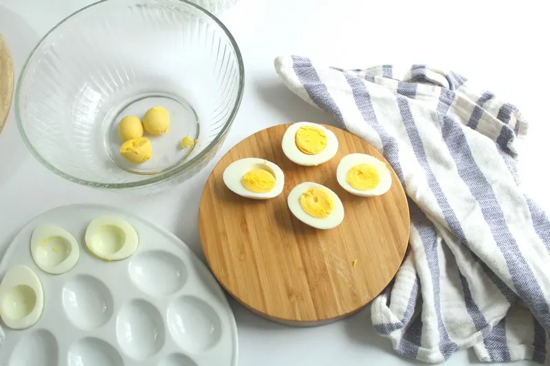 hard boiled eggs next to a bowl of a few egg yolks in process shot