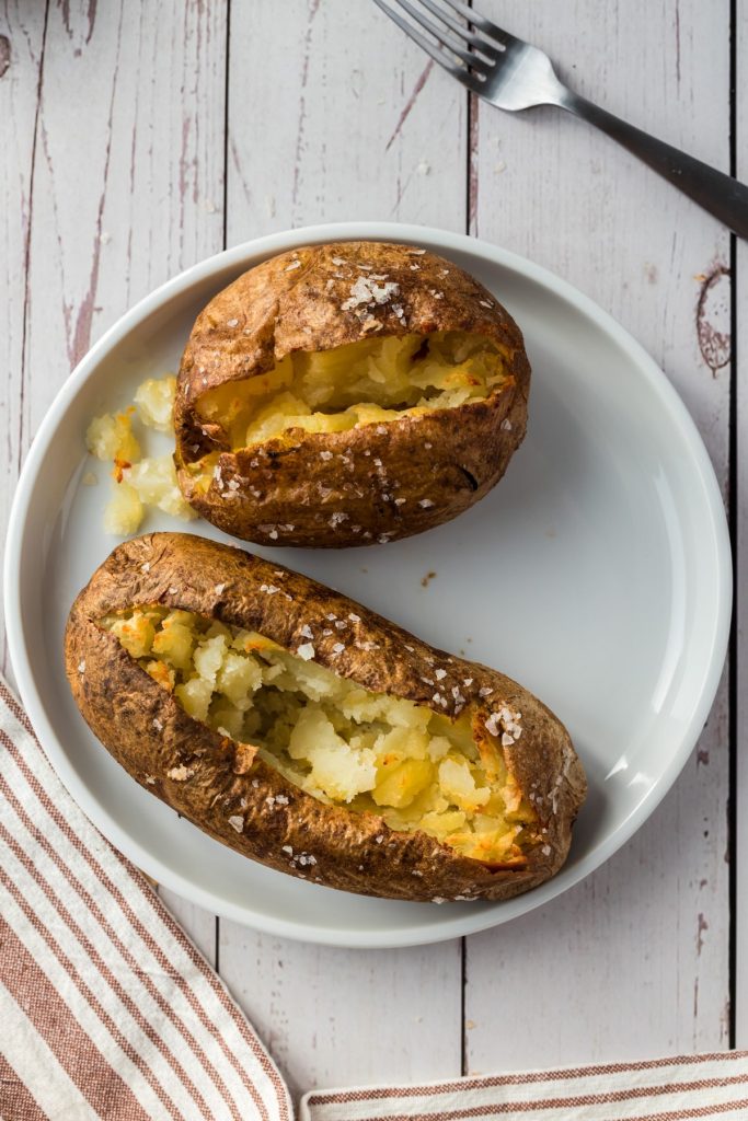 two baked potatoes on white plate with white background