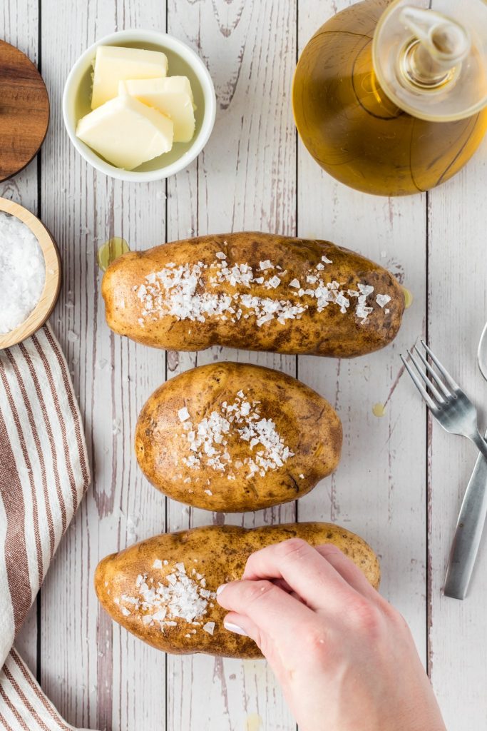 sprinkling salt on top of three potatoes