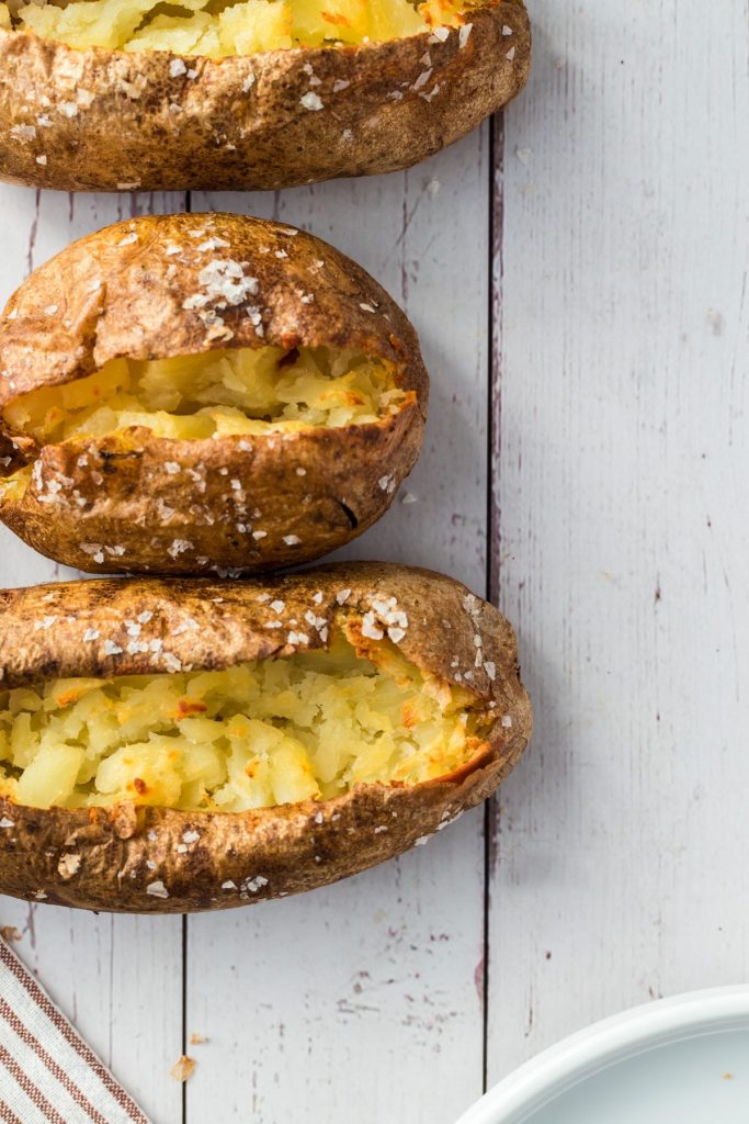 three baked potatoes on white wooden background