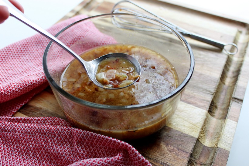 Spoonful of warm bacon dressing over bowl