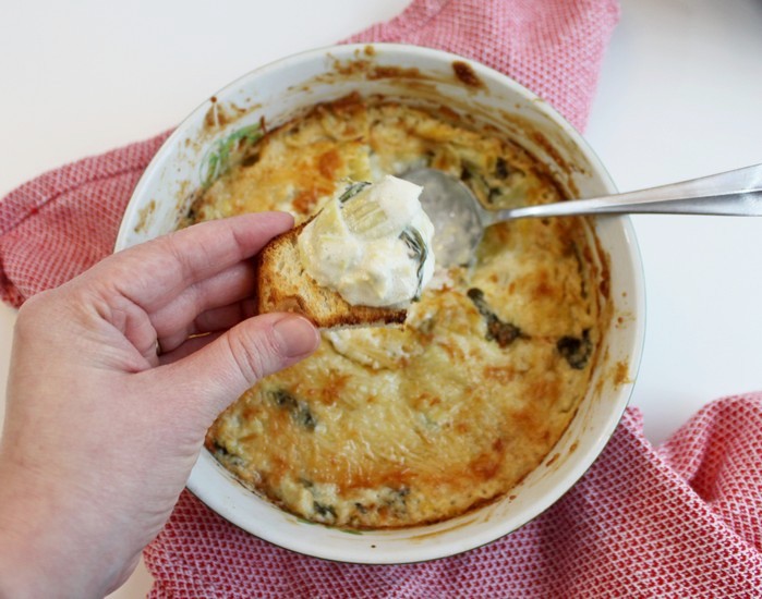 Spooning Baked Spinach and Artichoke Dip on bread