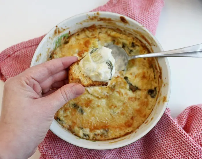 Spooning Baked Spinach and Artichoke Dip on bread