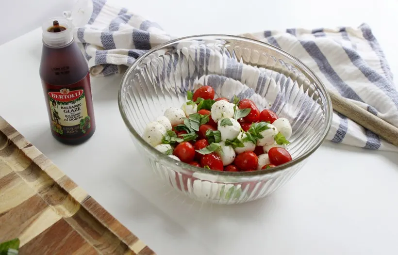 Mozzarella balls and tomatoes in bowl with basil and balsamic glaze