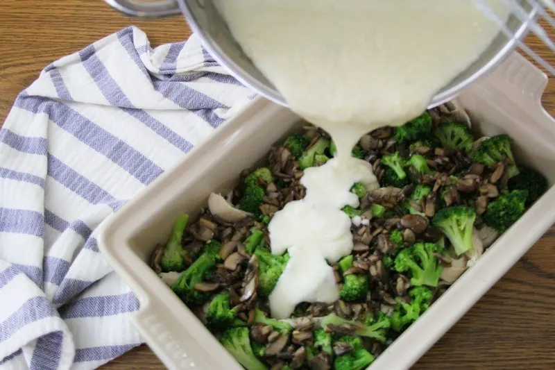 Pouring cheese sauce over mushrooms, broccoli and chicken