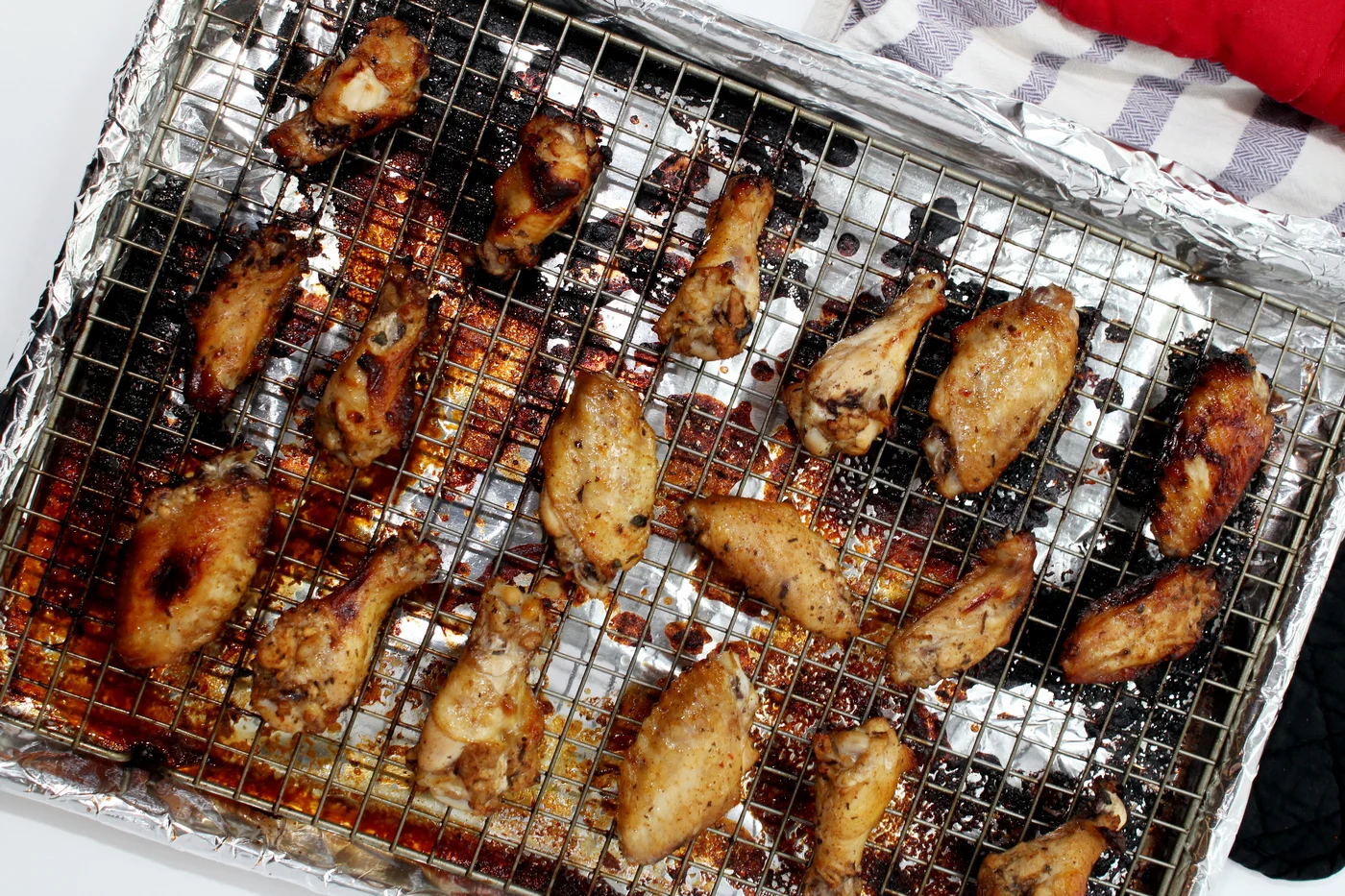 These chicken wings are tender on the inside and covered with perfectly sticky BBQ sauce on the outside. Nothing quite says gameday like these oven-baked wings! #wings #chickenwings #bakedwings #bakedchickenwings #recipe #easyrecipe #appetizers #appetizerrecipes #appetizerseasy #appetizersforparty #gamedayrecipes #gamedayfood Chicken wings on a baking sheet with towel
