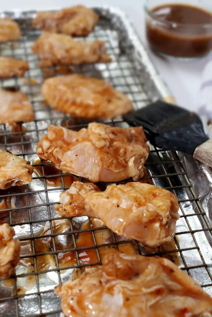 These chicken wings are tender on the inside and covered with perfectly sticky BBQ sauce on the outside. Nothing quite says gameday like these oven-baked wings! #wings #chickenwings #bakedwings #bakedchickenwings #recipe #easyrecipe #appetizers #appetizerrecipes #appetizerseasy #appetizersforparty #gamedayrecipes #gamedayfood Raw chicken wings on a baking sheet