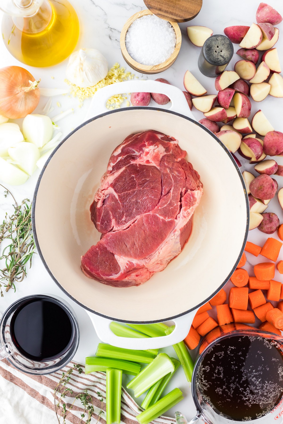 uncooked chuck roast in dutch oven surrounded by vegetables