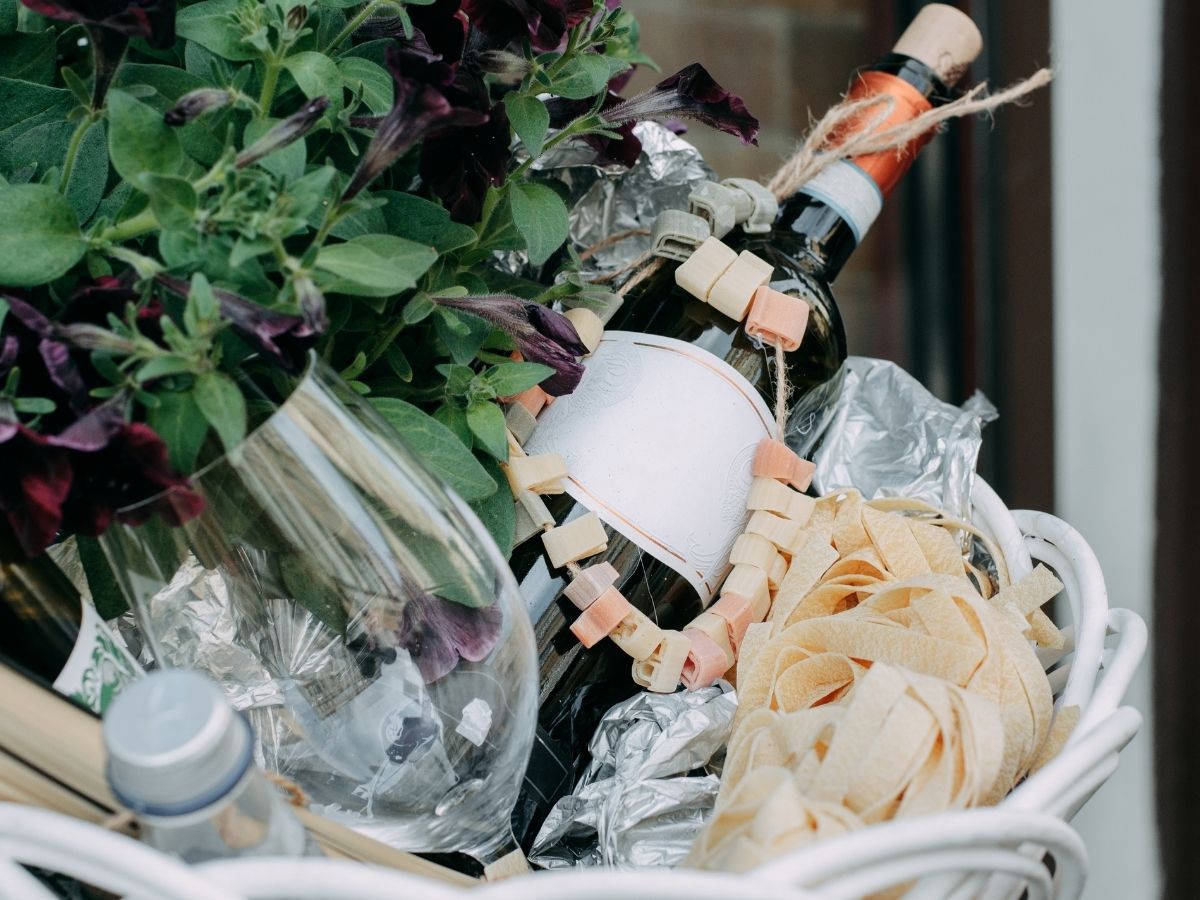 подарочная корзина с сушеными макаронами, цветами и бутылкой вина