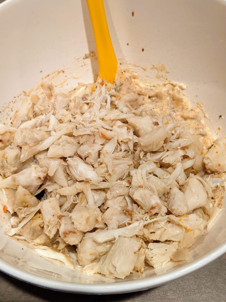 Lumb crab meat in mixing bowl with ingredients for crab cakes