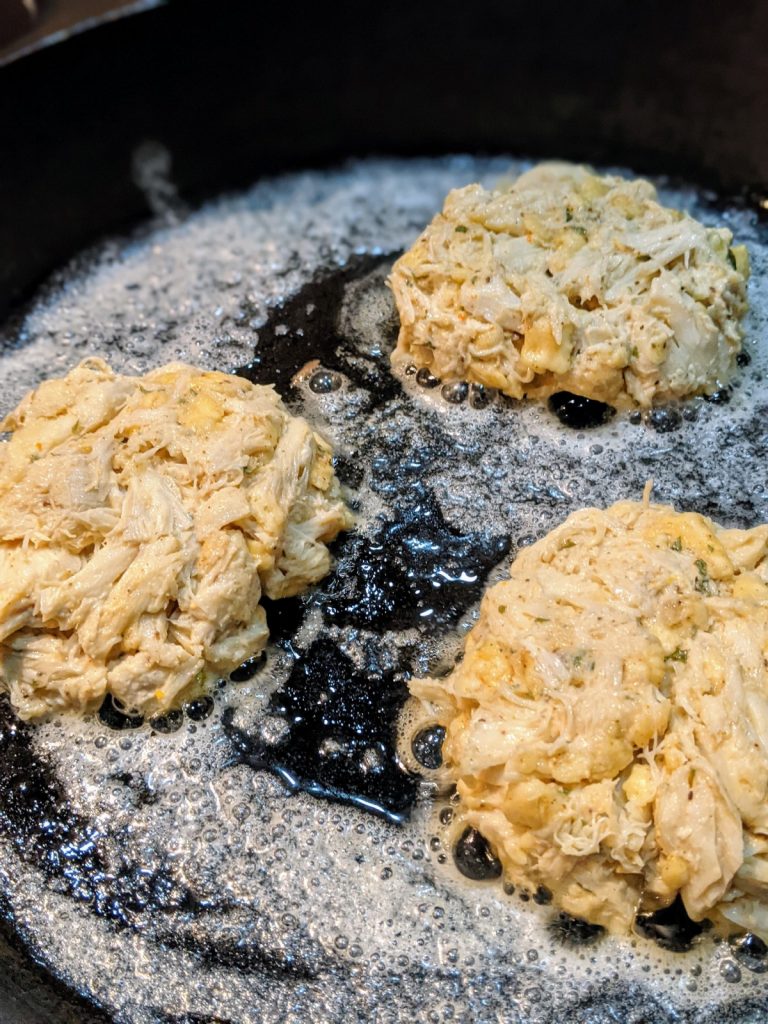 Crab cakes just placed in skillet. uncooked on top