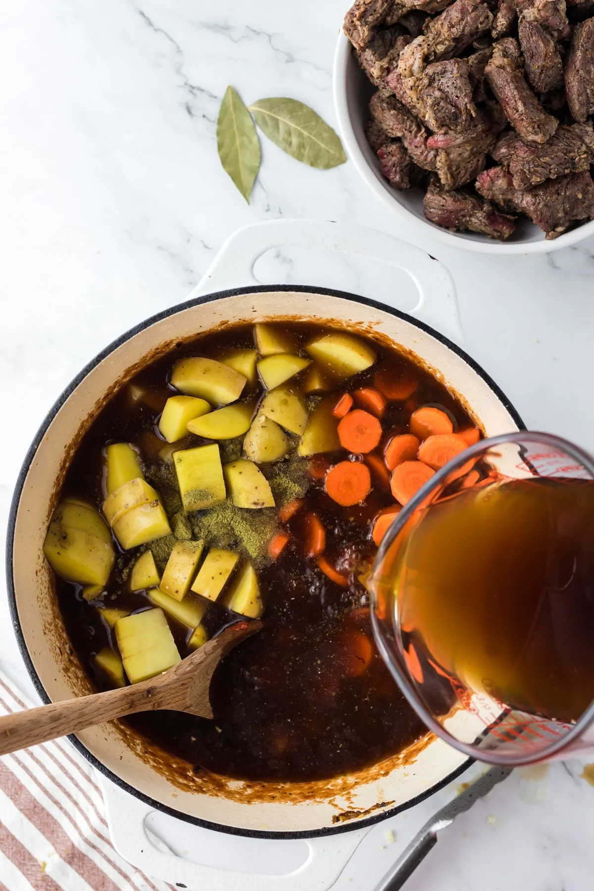 adding broth to beef stew ingredients in large pot