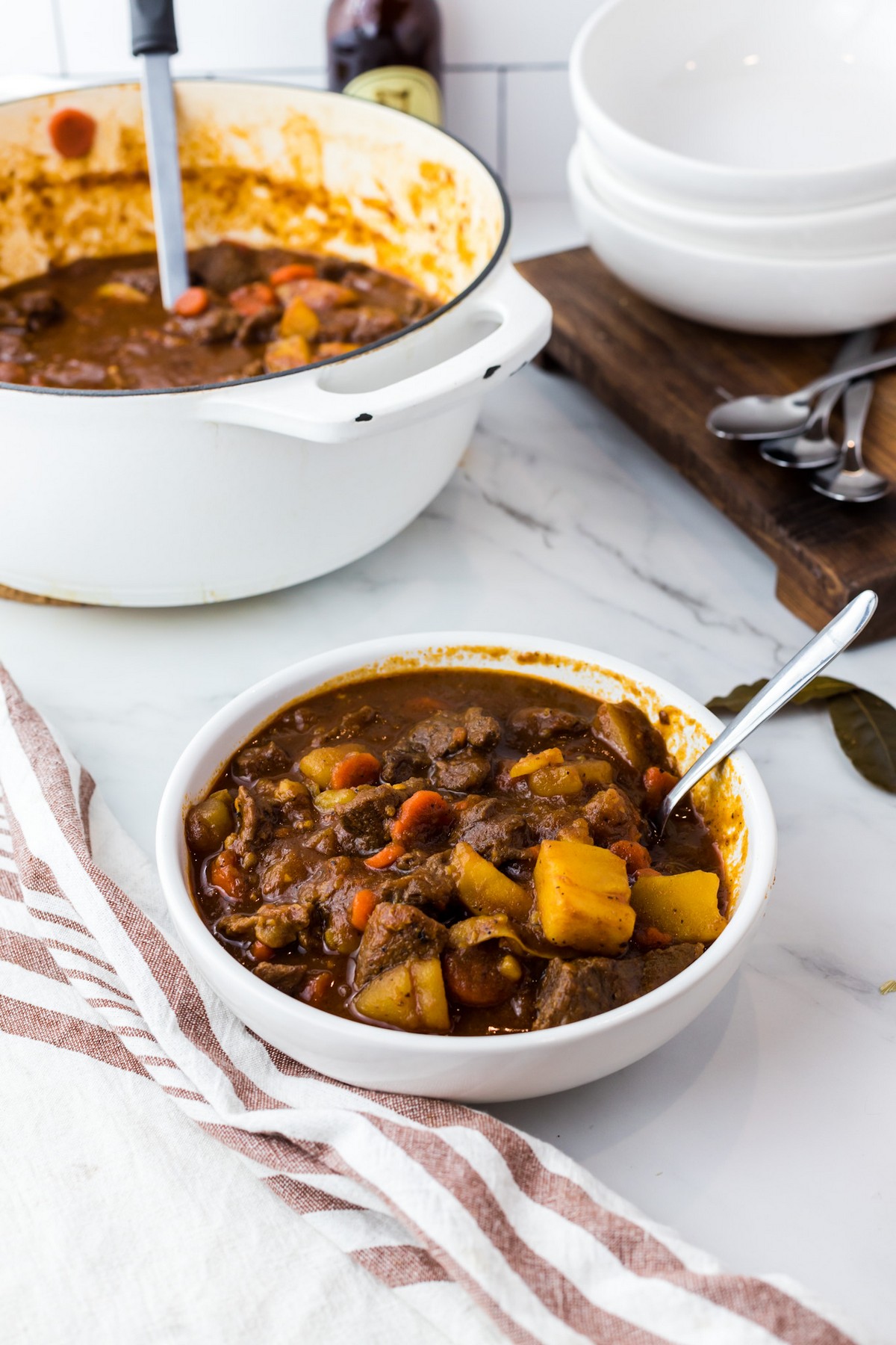 beef stew in single white bowl with dutch oven in background