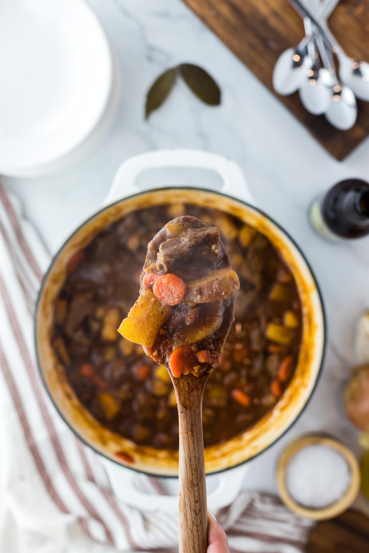 spoon of cooked beef stew ingredients over large pot