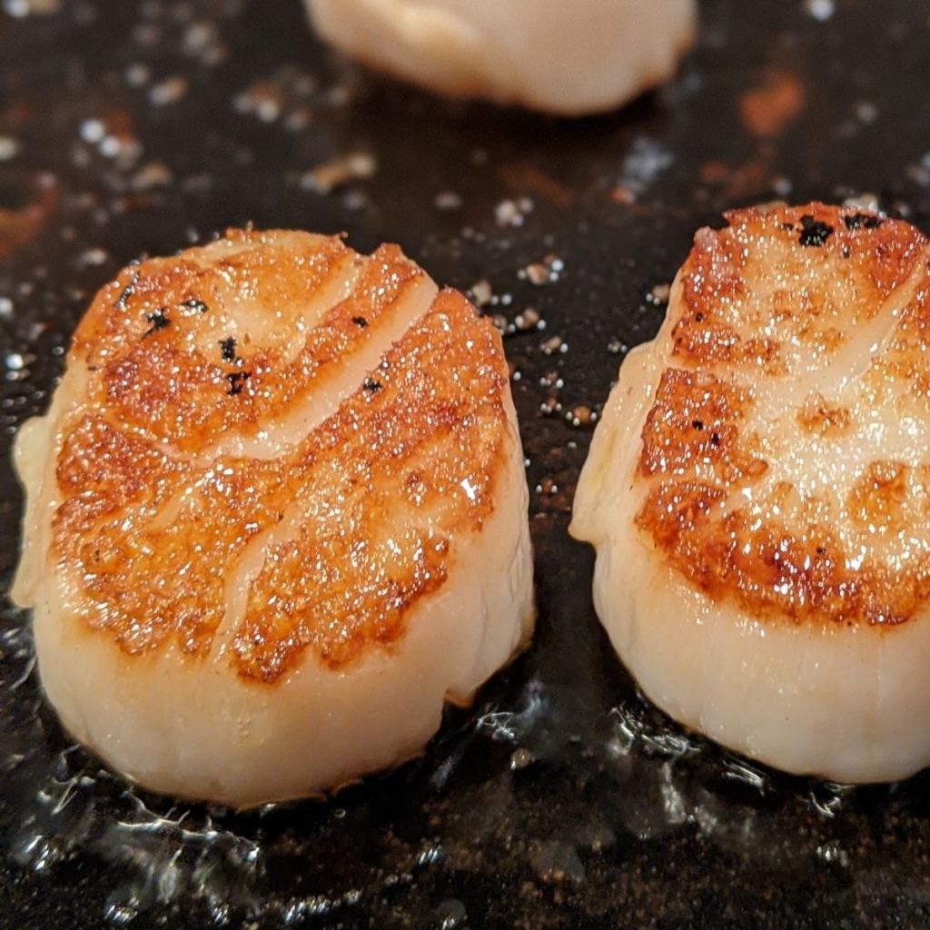 Two seared scallops on cast iron pan