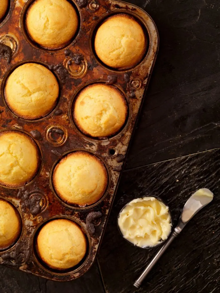 Corn muffins in baking tin with cup of butter on dark background