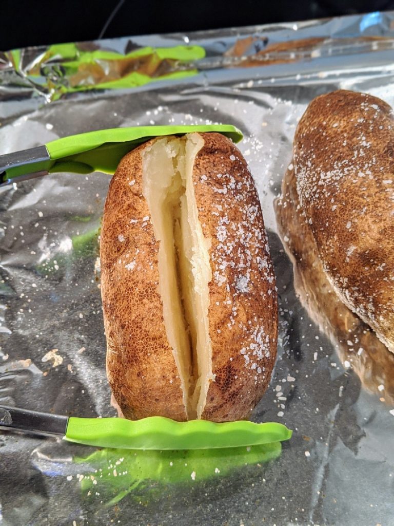 split baked potato held open with tongs
