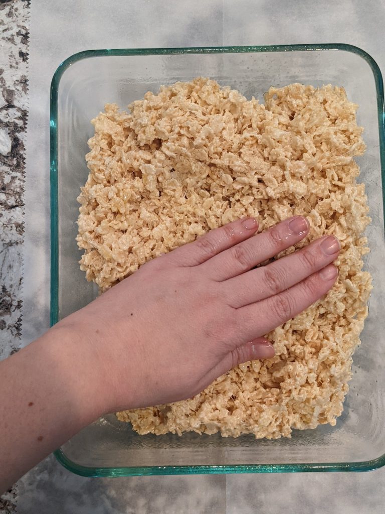 patting rice krispie treats mixture into dish