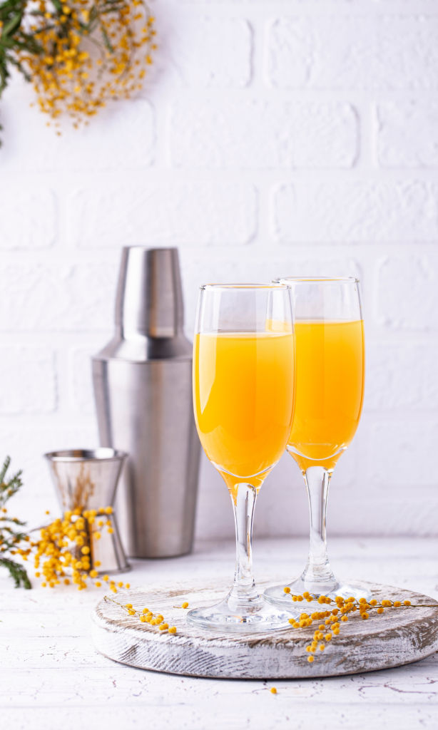 mimosa beverages in champagne flutes with cocktail mixer set in backgroun
