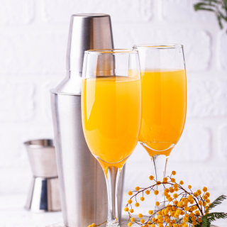 mimosa beverages in champagne flutes with shaker in background