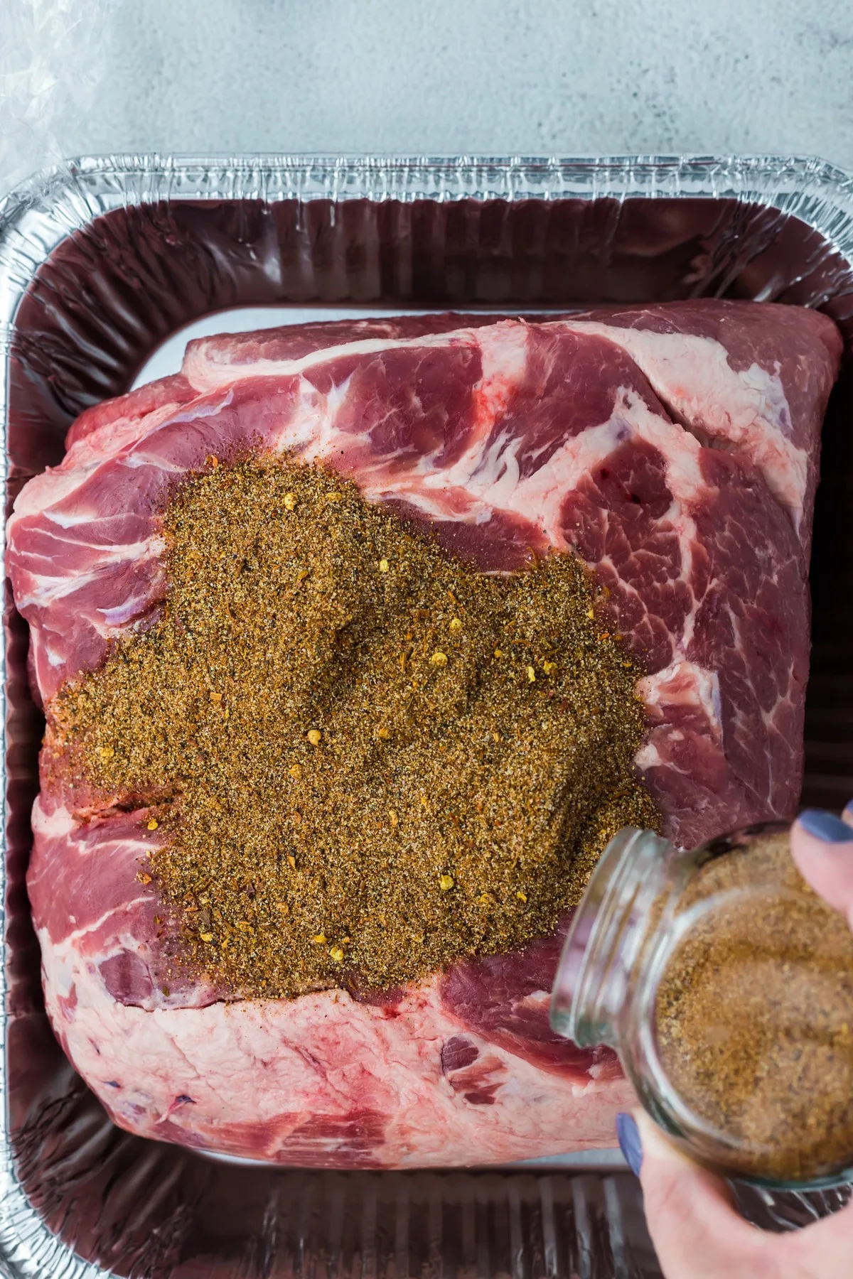 adding seasoning to pork shoulder