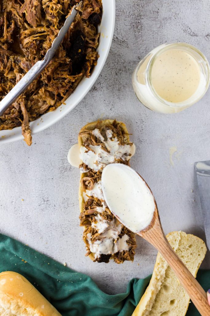 drizzling white sauce on bbq sandwich