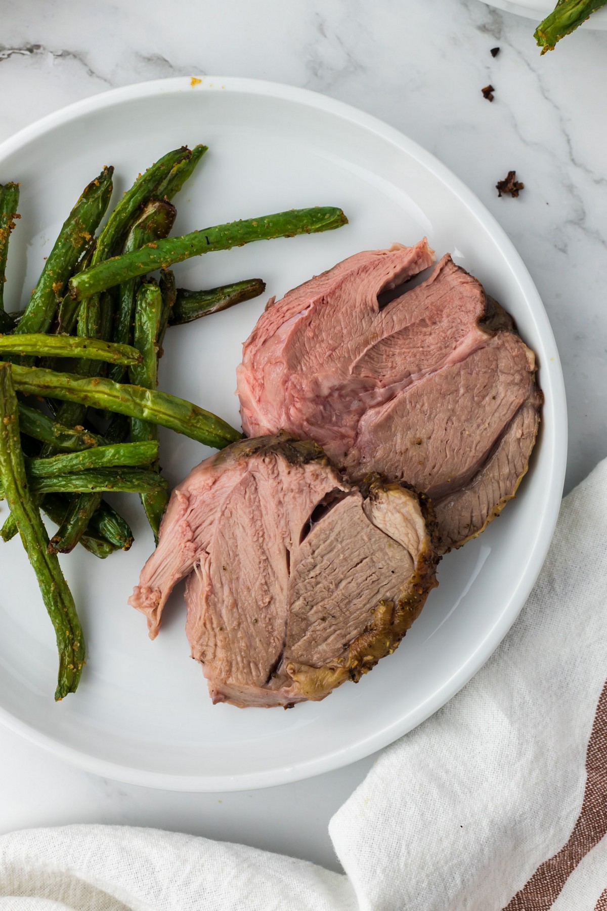 sliced lamb on white plate with green beans