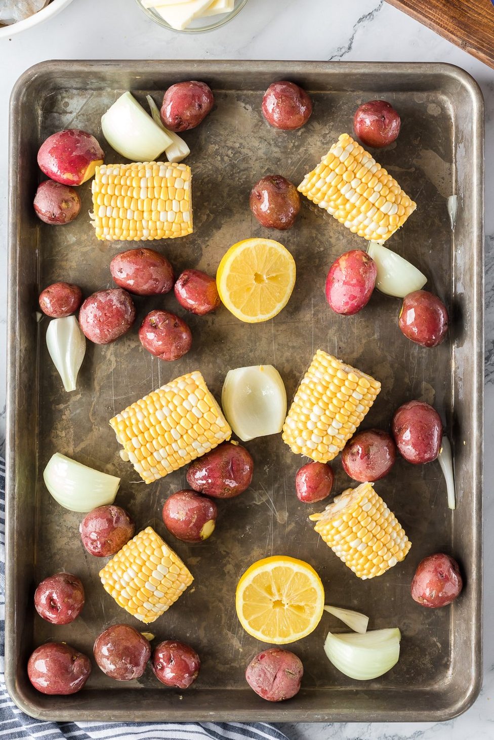 sheet pan of uncooked lemon, corn, potatoes, and onion.