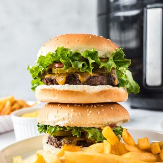 two burgers stacked on a plate with french fries