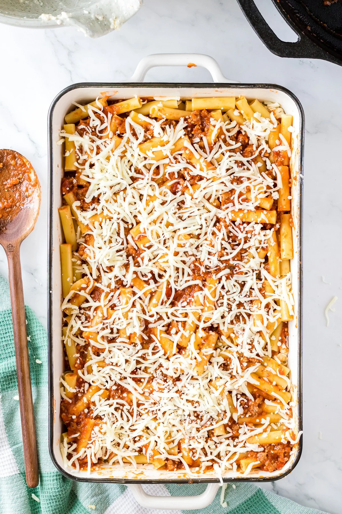 adding shredded cheese to baked ziti