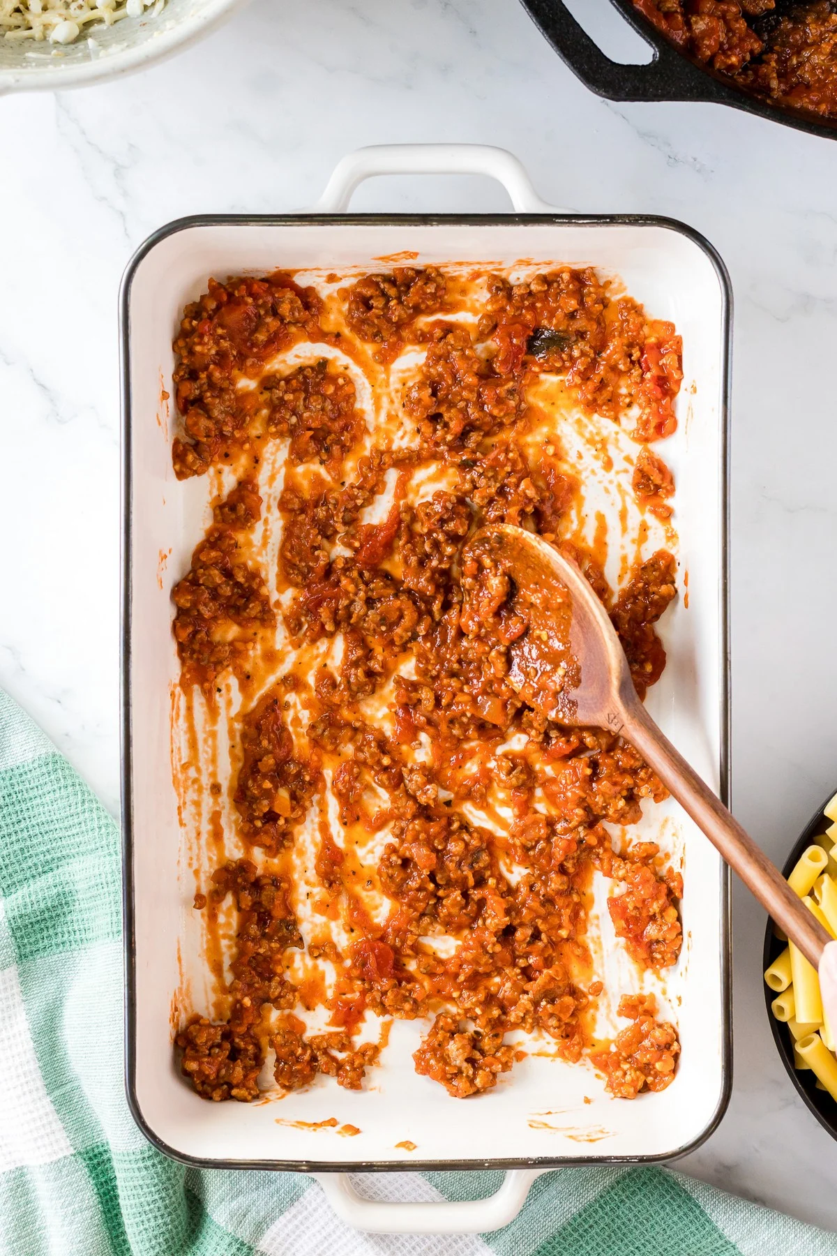 adding baked ziti meat sauce to casserole dish