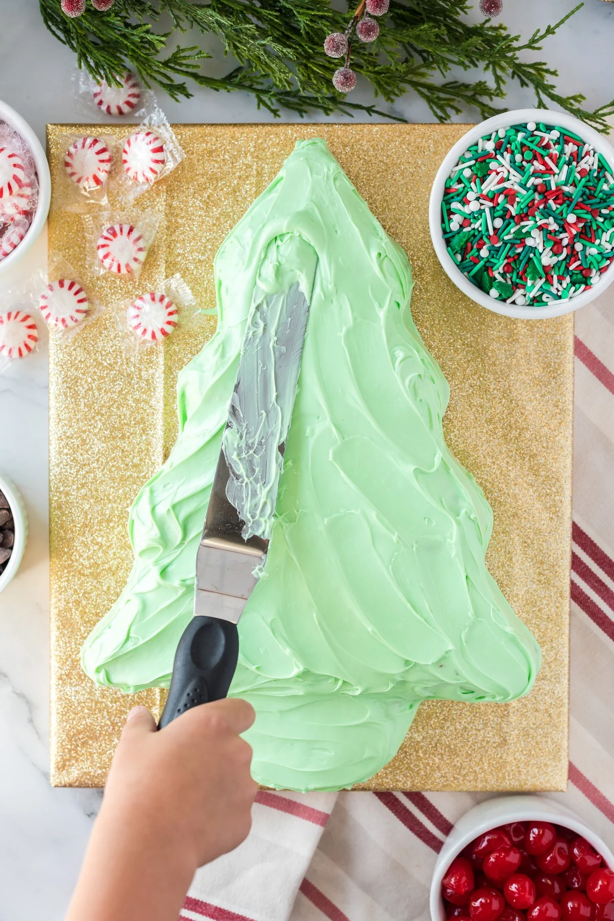 spreading green icing on baked christmas tree cake