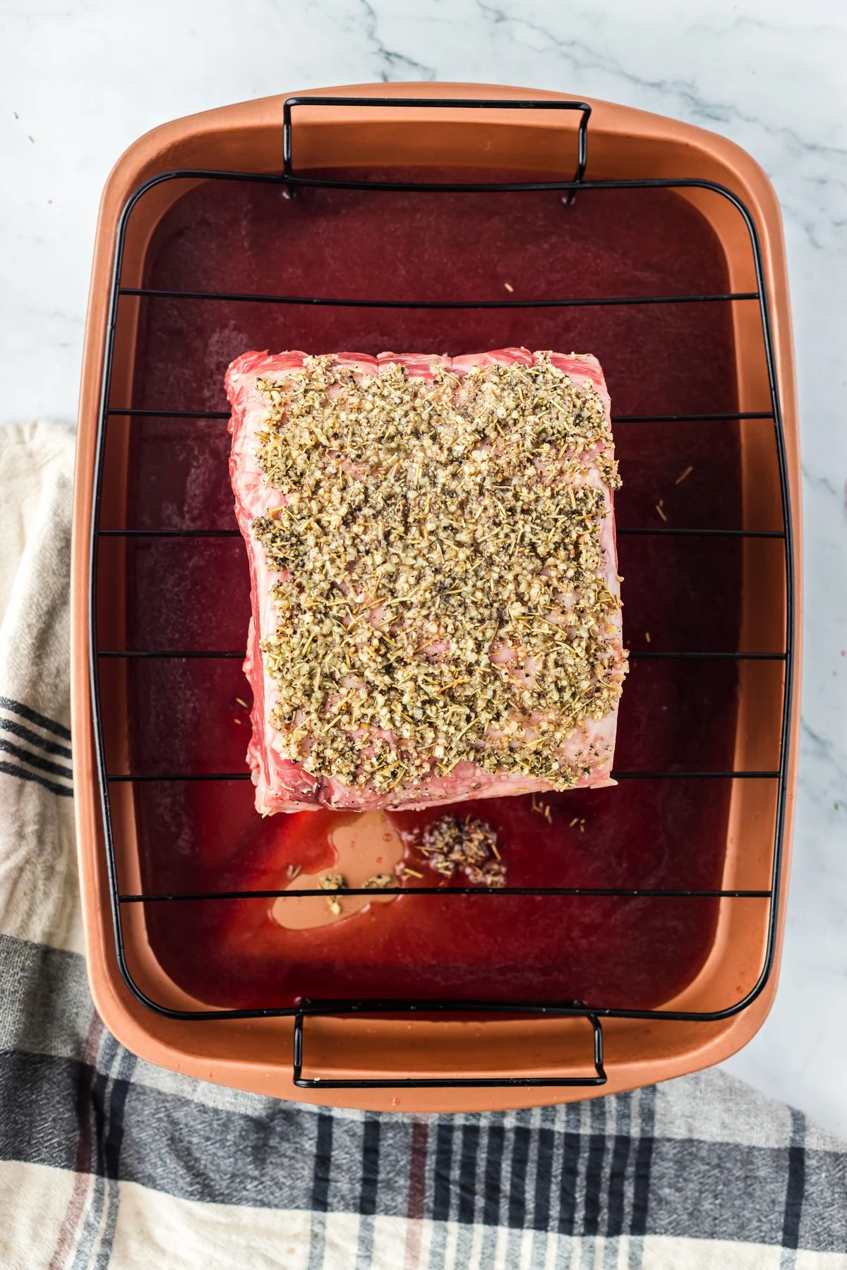 side angle of uncooked prime rib in roasting pan with seasoning