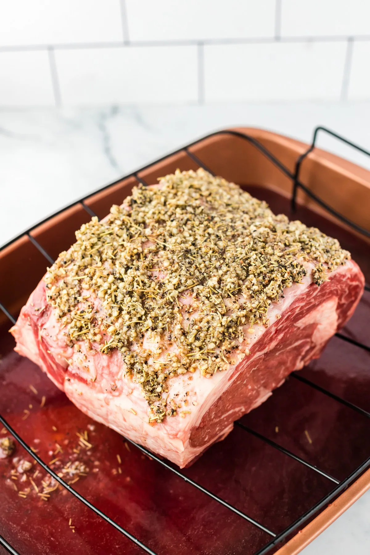 uncooked prime rib in roasting pan with seasoning