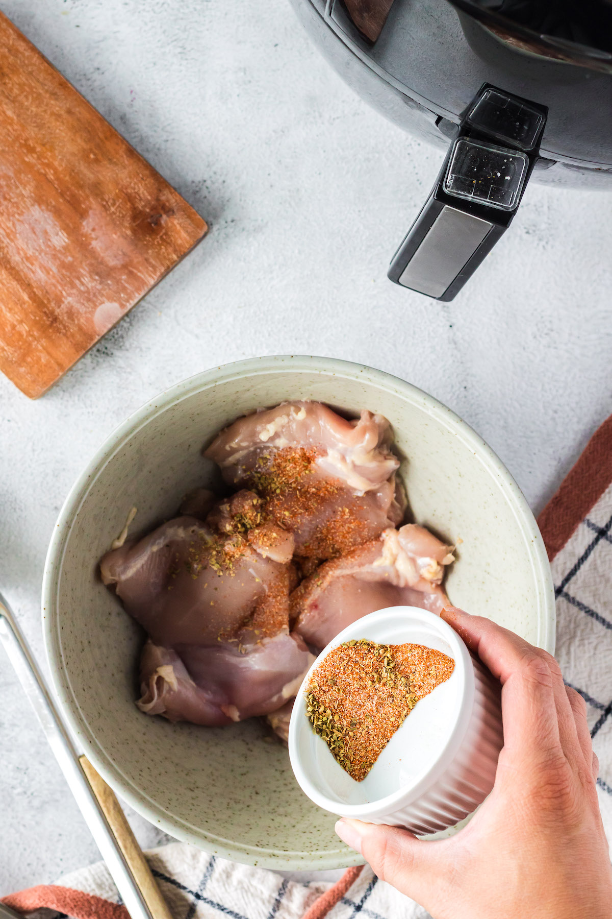 adding seasoning to chicken thighs in a bowl