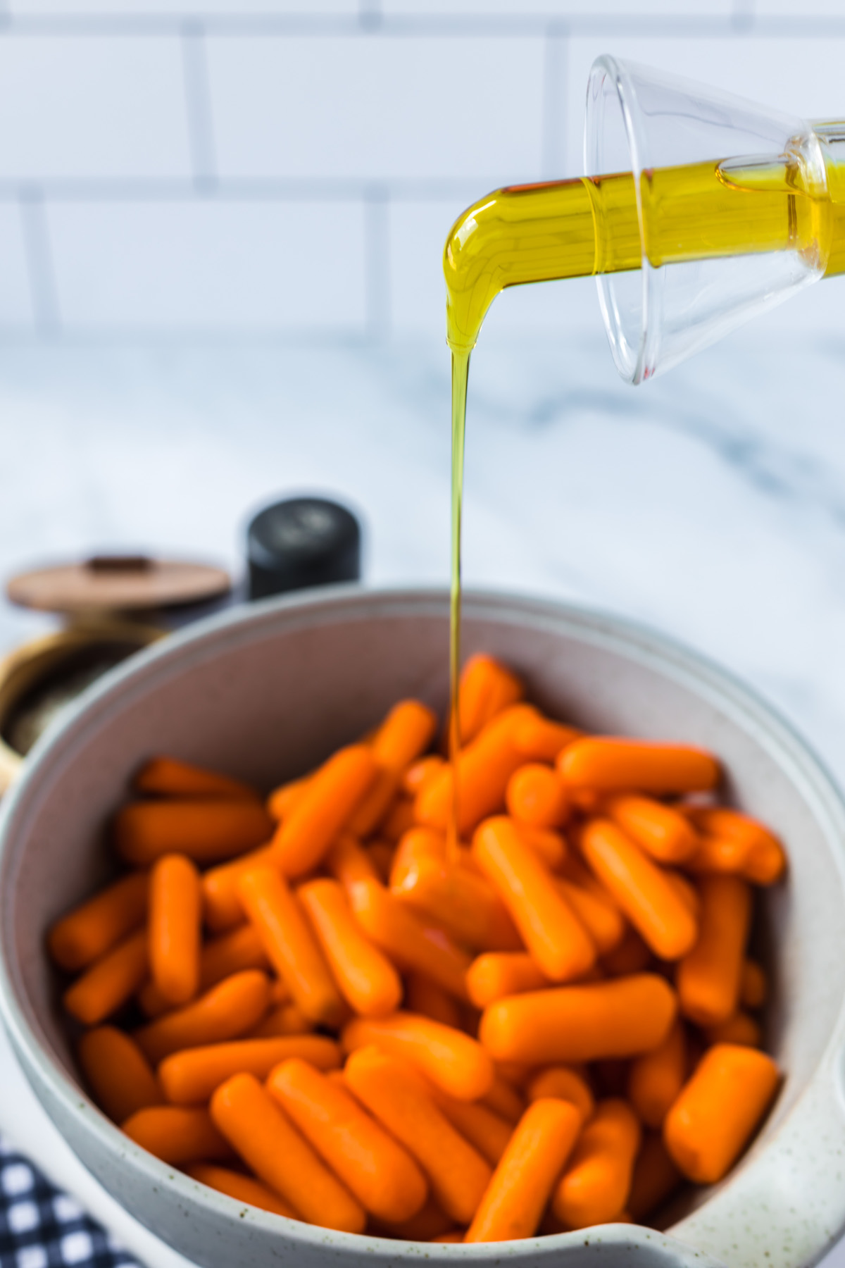 adding olive oil to bowl of baby carrots for roasting in the oven