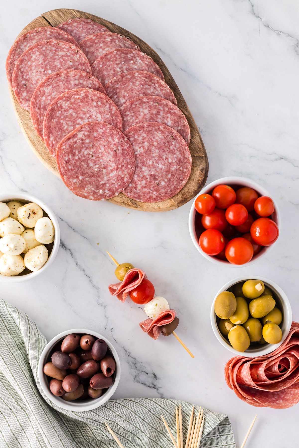 adding meats, olives, cheeses, and vegetables to charcuterie skewer