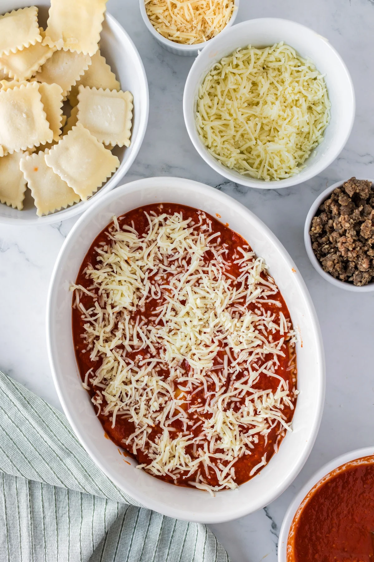 covering baked ravioli with shredded white cheese