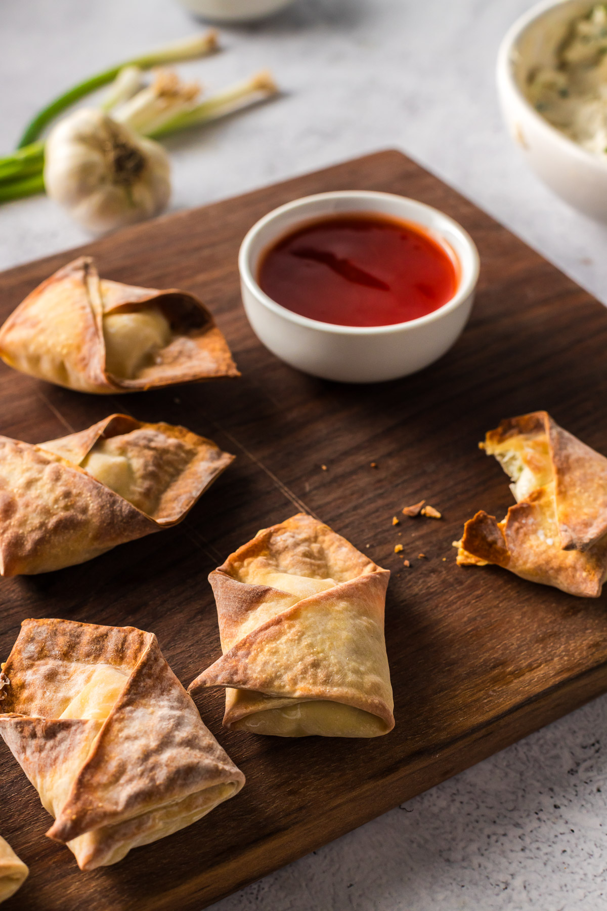 crab rangoon on cutting board with sweet and sour sauce for dipping