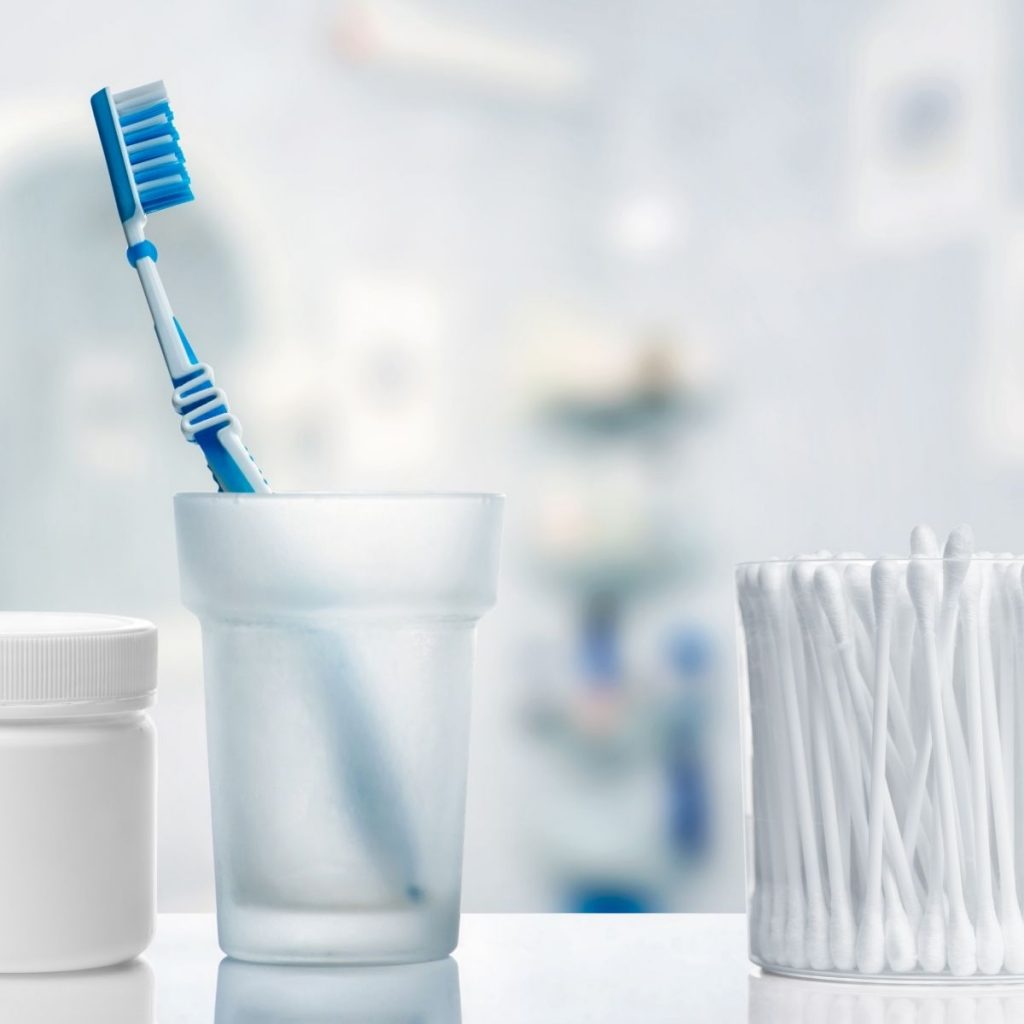 toothbrush in glass cup next to qtips