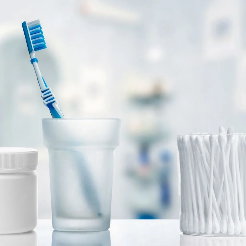 toothbrush in glass cup next to qtips