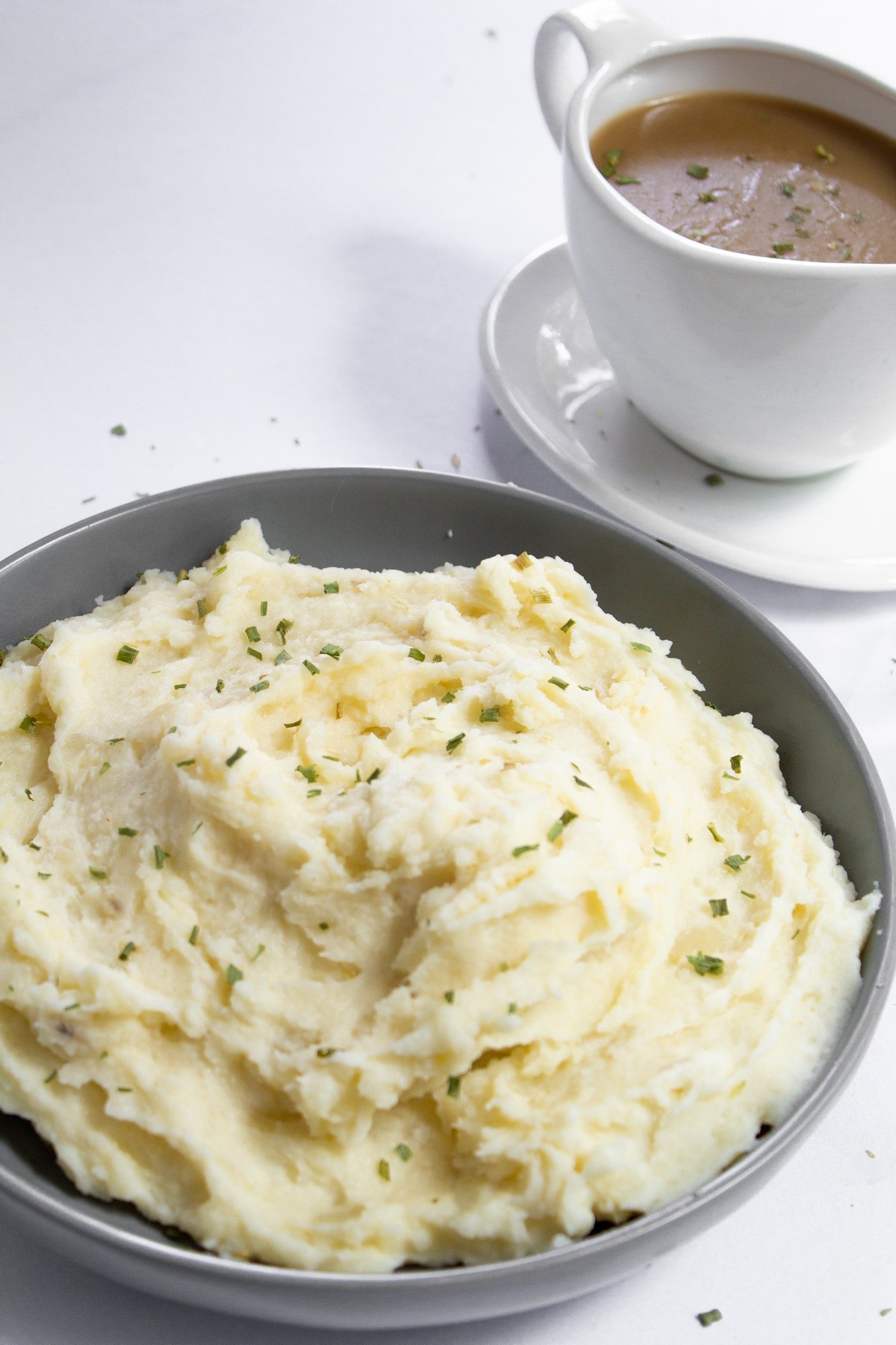 mashed potatoes garnished with chives and gravy in the background