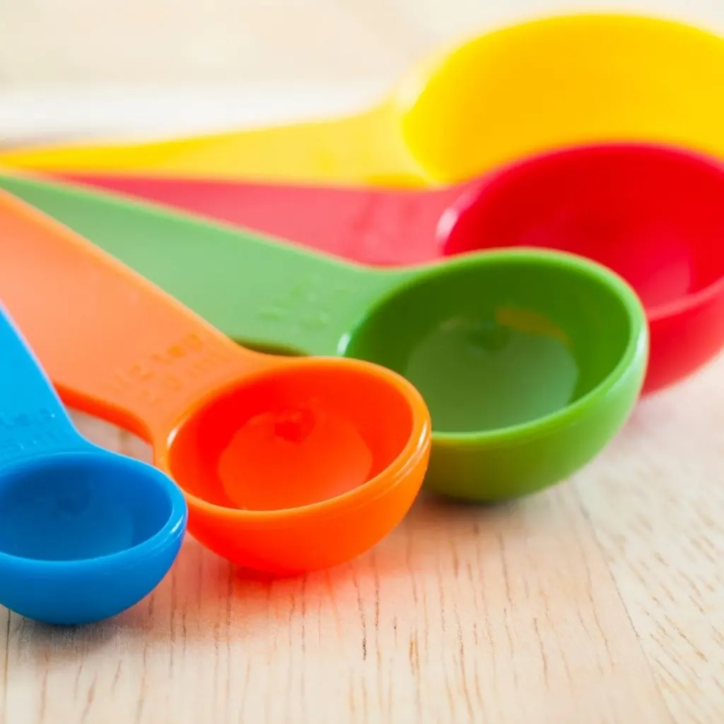 Colorful measuring spoons on wooden board